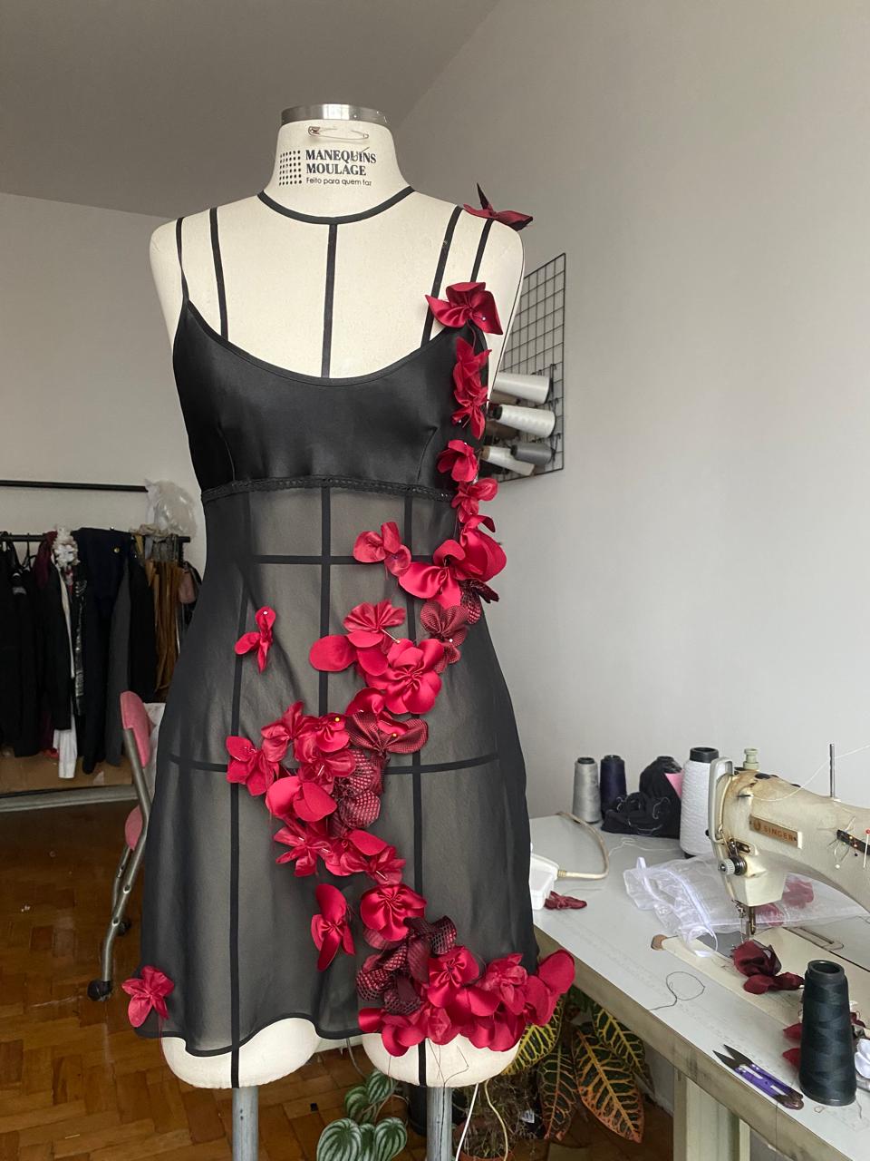 A black sheer dress with handmade red flowers in development on a studio dress form
